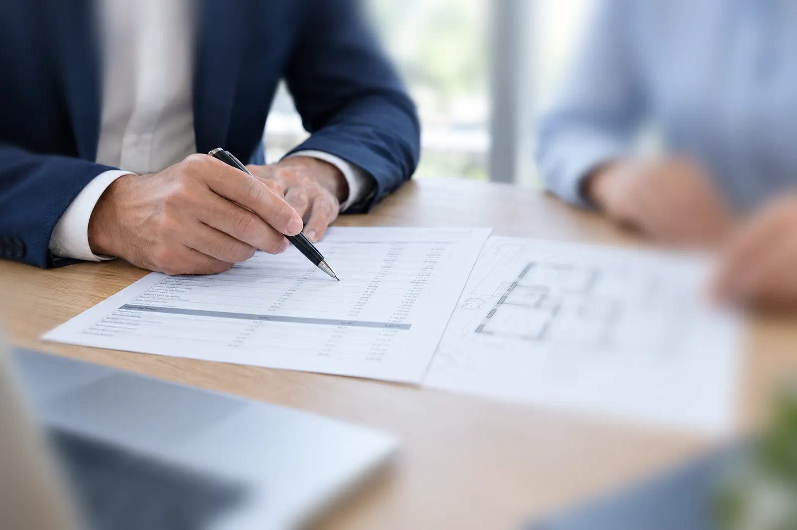 A consultant going through a builder’s quotation line by line with a pen, beside a floor plan